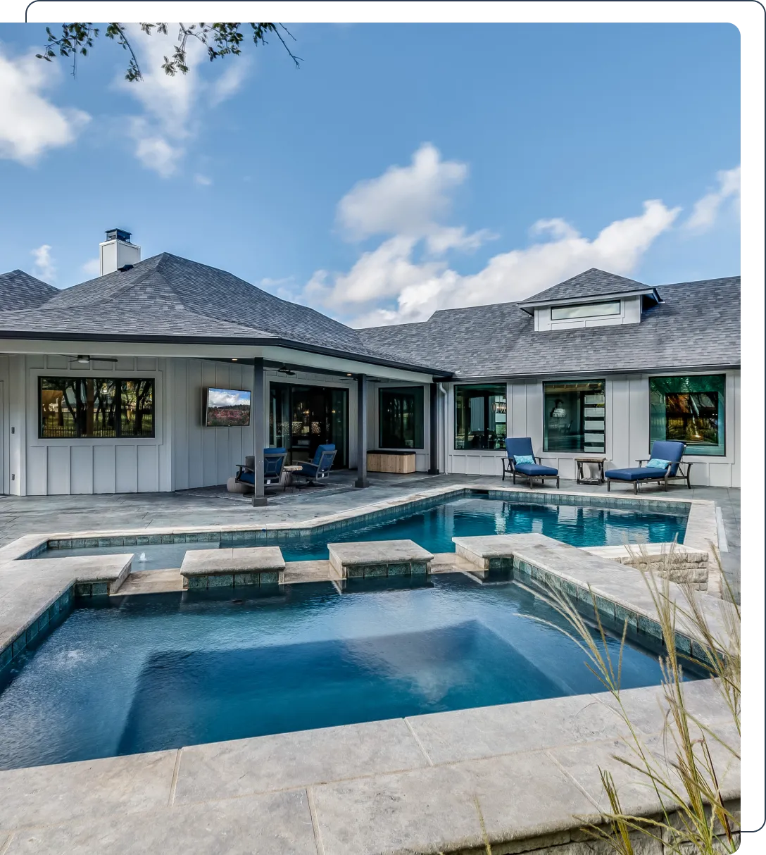 Modern house with a gray roof, featuring a backyard pool and hot tub. The outdoor area includes lounge chairs and a covered patio with a TV.